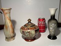Three items shown side by side with a Coca-Cola can for size reference: stone carved vase, vintage Satsuma ginger jar with lid, and ceramic vase with floral design.