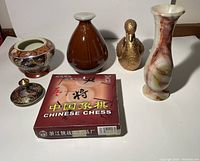 Overview of the full lot showing the Satsuma bowl with lid, brown vase, brass duck figurine, marble-effect vase, and boxed Chinese chess set.