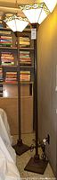 Two tall floor lamps side-by-side against a wall with bookshelves in background.