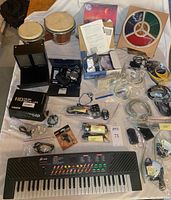 Full view of lot laid out on a flat surface showing digital keyboard, bongo drums, speakers, cameras, cords, and game box