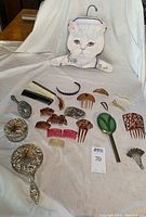 Full view of the silver plated vanity set items including hand mirror, brushes, powder container, nurse cat hanger, and various vintage hair combs scattered around