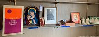 Wide shot of shelf displaying various Catholic decorative items including a colorful wall hanging, stained glass icon, framed photo, nativity set, and other small religious pieces.