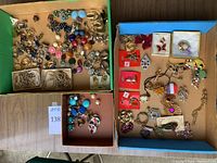 Overview of multiple compartments of box filled with assortment of clip-on earrings, pins, and strands of artificial pearls, some damaged.