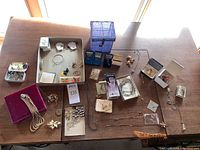 Full view of the assortment of jewelry on a wooden table showing necklaces, pins, a blue crystal ring holder box, and other pieces.