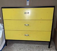 Front view of yellow-front three-drawer dresser in black frame