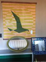 Overall view showing striped canvas and wood wall hanging with seagull design above green oval mirror and blue mosaic mirror.