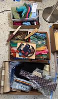 Photo showing assorted scarves, fans, mini glasses cases, and headbands arranged in boxes, highlighting variety in materials and colors.