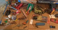 Wide shot showing assortment of vintage metal toys including toy vehicles, parts, and accessories laid out on cardboard.