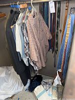 Gray wool trench coat hanging with dress shirts and casual clothing, gloves and caps visible below