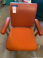 Front view of vintage orange office chair showing woven fabric seat, vinyl padded armrests and backrest, and metal caster base.