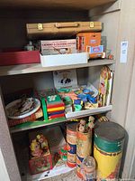 Shelf showing assorted toys including box with laundry and cleaning center toy, paper puppets, building blocks, and puzzles.
