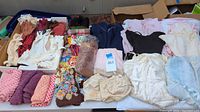Top-down photo of various vintage gloves, stockings, scarves, full slips, and pantaloons arranged on a table, showing textures and colors.