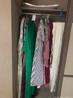 Several vintage women’s dresses hanging side by side in closet showing various patterns and colors including stripes, florals, madras plaid and solid tones.