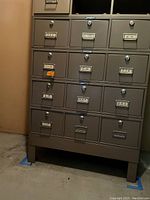Front view of bottom steel cabinet with multiple small drawers, labeled alphabetically, some missing drawers.