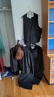 Photo shows a black paisley suit vest, Calvin Klein coat, Marvin Richards leather jacket, and brown leather-like fanny pack hanging on hangers and displayed together.