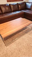 Photo of full coffee table placed in front of a brown leather sectional sofa on carpeted floor.