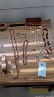 Overview of lot showing multiple necklaces, earrings, pen set in wooden case, brooch, and bracelet on wood table surface