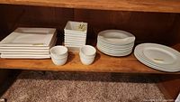 Wide shot showing all items: six square plates, three round plates, ten soup bowls, four ramekins, eight dessert bowls.