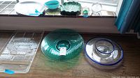 Image showing the assortment of glassware items including various trays, bowls, and paperweights arranged on a wooden surface near a window.