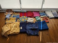 Full overhead view of assorted linens and cloth items including napkins, placemats, tablecloths, and two chef hats on wooden floor by window.