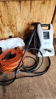 AR Blue Clean 240 pressure washer and orange extension cord reel in wooden shed.