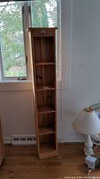 Full view of tall narrow wooden shelf unit positioned by window