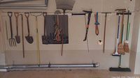 Full view of yard tools hung on a wall including shovels, rakes, weeder, brooms and specialized hand tool with pruning blades.