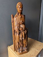 Front view of carved wooden statue showing Virgin Mary seated with child Jesus, highlighting detailed facial features and pleated robes.