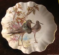 Front view of the scalloped white ceramic cabinet plate showing detailed hand-painted image of two birds with foliage and gold rim.