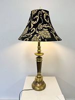 Front view of the tall brass table lamp with brocade patterned shade illuminated.