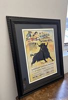 Framed Spanish Toros Festival Bull Fighting poster leaning against a window with visible reflections, showing the full front view of the artwork and frame.