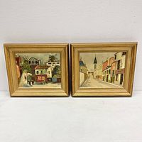 Front view of both framed Parisienne oil paintings showing street scenes in gold frames