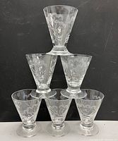 Group photo showing six clear etched cordial wine glasses stacked in a pyramid shape against a black background.