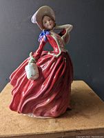 Front angle showing the woman's face, bonnet, red dress, and basket held in right hand.
