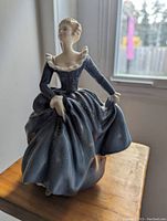 Front view of Royal Doulton lady figurine in blue gown on wooden surface, showing detailed facial features and dress