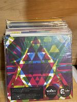 Stack of vinyl records in their sleeves showing colorful geometric cover art on top record