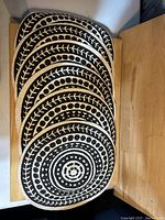Stack of six round fabric place mats displaying black and white concentric pattern with leaves and dots.