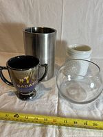 Photo shows four decor items: metal wine chiller, white ceramic vase, clear glass bowl, and trophy-shaped cup with text.