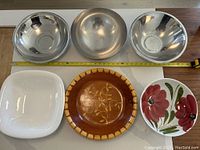 Top front view showing all six bowls arranged in two rows: three metal bowls in top row and one white ceramic, one wooden with inlay, and one floral ceramic bowl in bottom row.