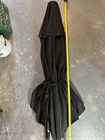 Full view of black patio umbrella in closed position with a measuring tape beside showing approximate height of 96 inches.