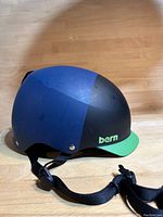 Front side view of the brimmed snowboard helmet showing the blue and black shell with green brim and 'bern' branding.