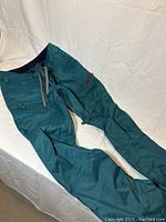Full view of the green Burton women’s snowboard pants laid out flat showing the design, zippers, and adjustable waist.