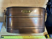 Top view of the oval brushed bronze metal storage bin with a Smith & Hawken brand plaque.