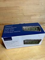 Photo of the original boxed Insignia Digital AM/FM Clock Radio. Box shows product name, image of the clock radio with LED time display 10:30, and bilingual description.