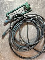 Photo of coiled black and blue garden hose with green oscillating sprinkler attached, on a concrete floor.