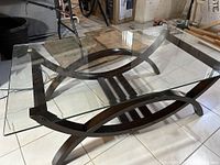 Glass coffee table with metal base viewed at an angle showing the decorative metal frame and thick clear glass top.