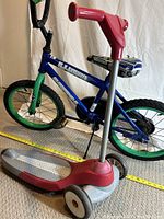 Blue and green kids bike with visible tears on the seat and red scooter with gray standing deck and red handlebar in front