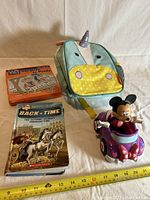 Front view of the set showing the unicorn backpack, children's book, game tin box, and Minnie Mouse toy car on white background with measuring tape below.