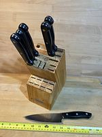 Knife block with six knives inserted and one knife laid out in front for scale