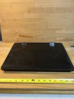 Front view of black laptop lap tray placed against wooden background with ruler measuring about 15 inches width